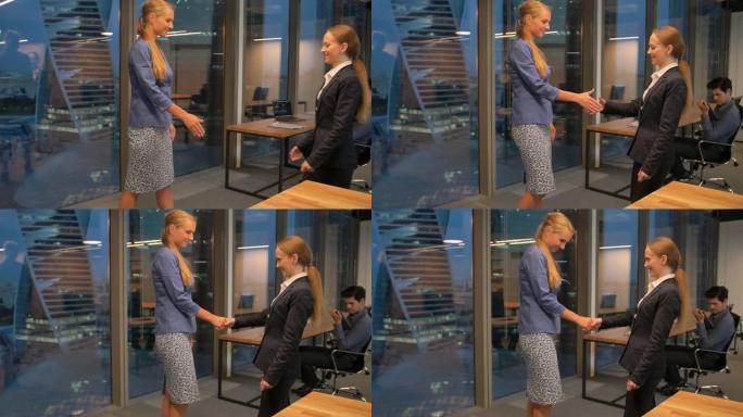 两个快乐的年轻女商人在现代商务办公室内握手