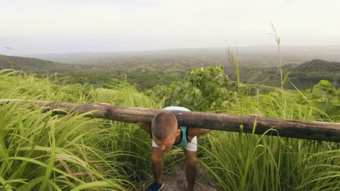 健美运动员训练斜坡，肩膀上有沉重的木条，在野生自然景观上。男子在户外举重健身房使用木棒。热带地区的运