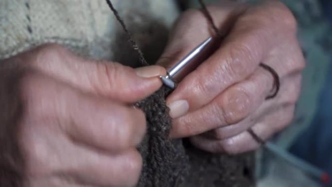 极端特写，一位资深人士编织精美而美观，紧闭一位奶奶的双手，上面满是皱纹，正在制作一件新的冬季毛衣，活