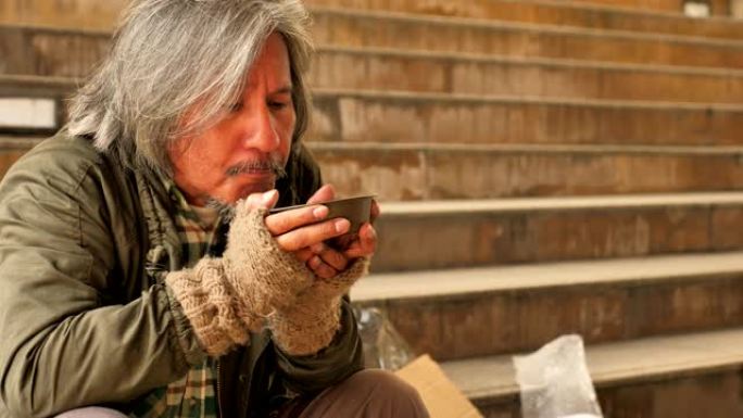 无家可归的老人坐在城市的楼梯上吃着志愿者的汤