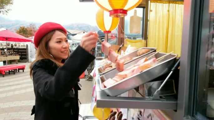 在日本街头市场，一名亚洲妇女从食品卡车上选择烤肉串 (烤猪肉) 的4k移动镜头