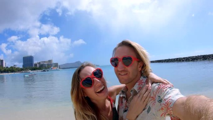 一对夫妇在夏威夷檀香山的威基基海滩自拍。威基基海滩的自拍视角广角。年轻夫妇用心形太阳镜自拍