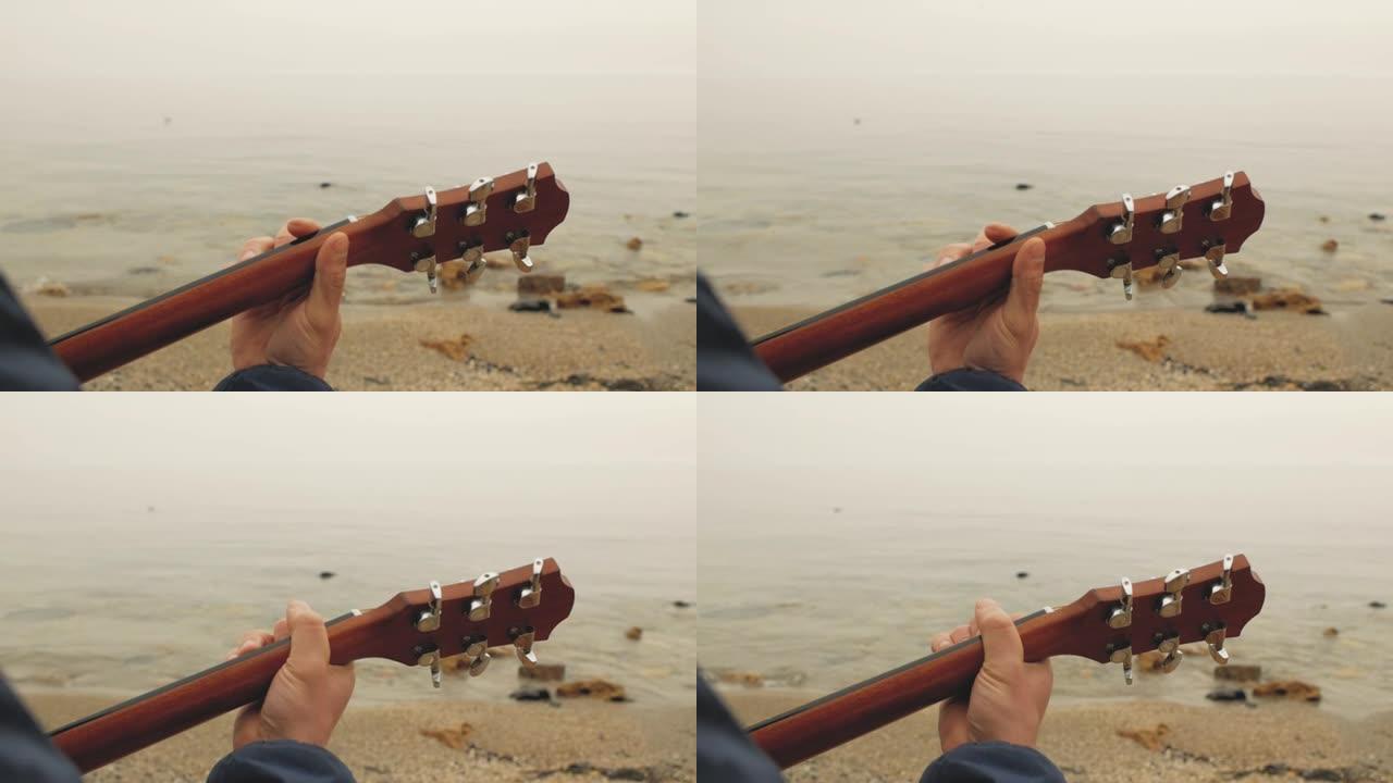 男性手在大海的背景下弹奏吉他上的和弦。弹吉他后视图