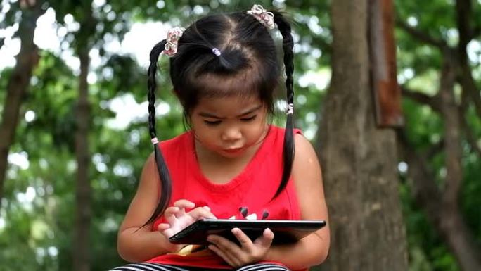 Asian gilr正在公园的平板电脑上玩游戏。女孩使用平板电脑。