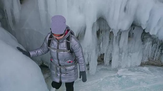 女人在贝加尔湖冰上的旅行。去冬日岛旅行。女孩正走在冰石脚下。旅行者看着美丽的冰窟。极度跋涉和行走。背