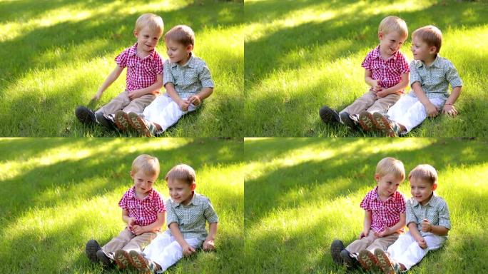两个有趣的小男孩在公园的绿草地上玩耍，他们坐在草地上