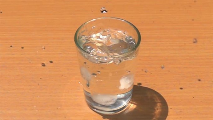 将自制的冰块放入木制桌子上装满淡水的玻璃杯中