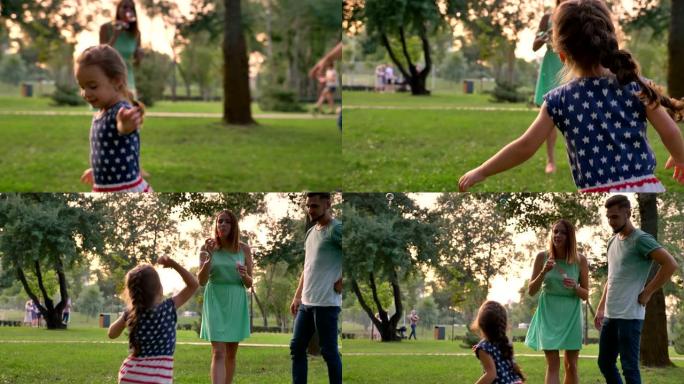 年轻的家庭夏天在公园散步，女儿在抓泡泡，童年的概念