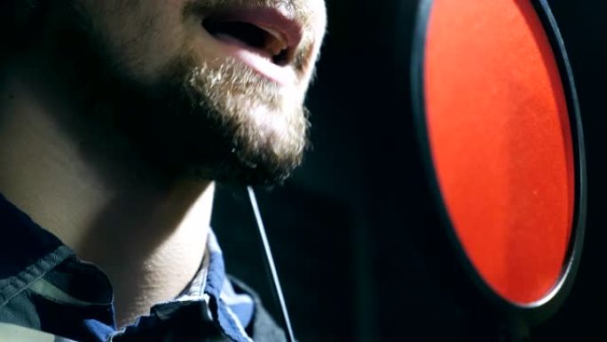 在sound studio中，男歌手戴着耳机在麦克风中演唱歌曲。年轻人在情感上录制新歌。创意音乐家的