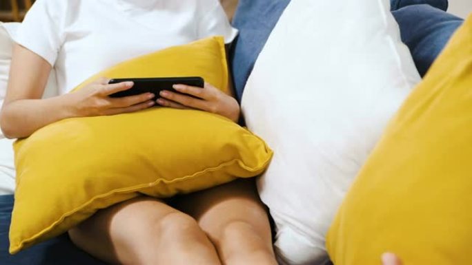 关闭亚洲妇女坐在沙发上使用手机在线在家令人不寒而栗。数字时代的生活方式