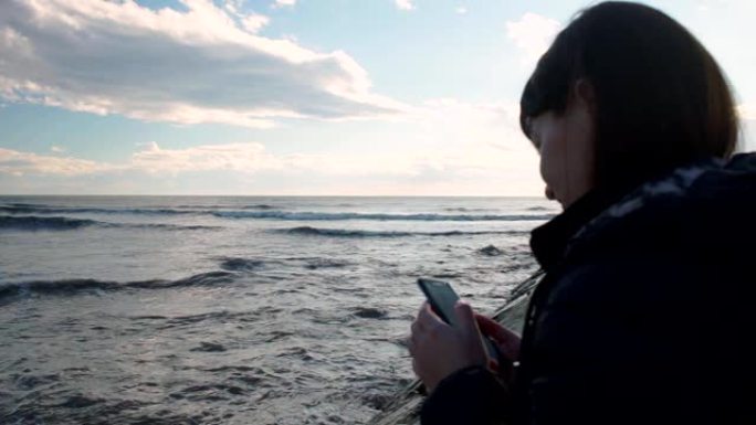 年轻女孩站在海边，看着智能手机
