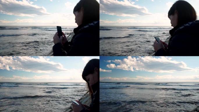 年轻女孩站在海边，看着智能手机