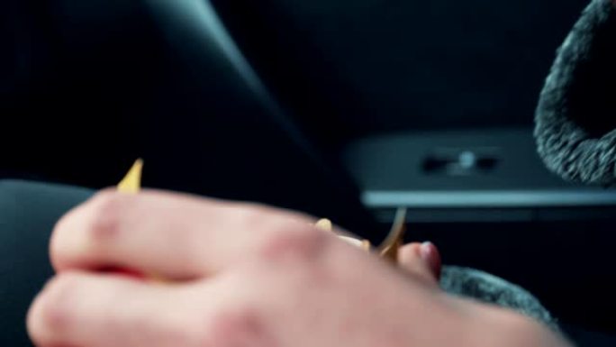 年轻女子的特写镜头用手指拿薯条，然后在汽车上吃