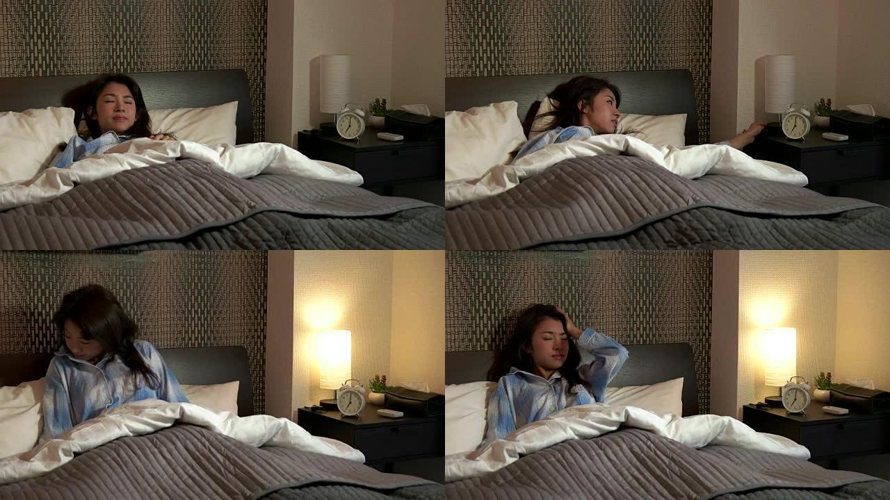 漂亮的亚洲女人在家里的卧室里。清晨的例行公事，疲倦的日本女孩在床上醒来，打sn闹钟并打开灯。人与生活