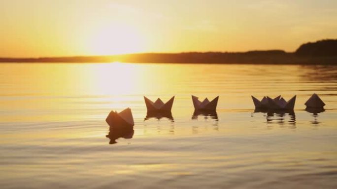 许多漂亮的自制纸船漂浮在河里，有着美丽的日落背景。
