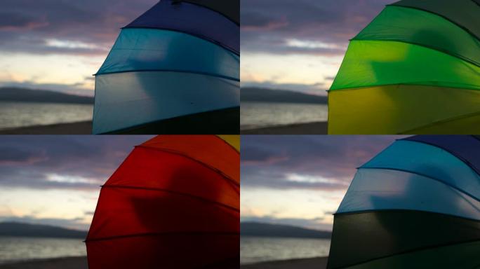 日落时在沙滩上旋转彩虹伞的女人