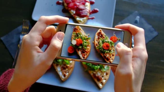 俯视图-女人的手使用智能手机拍摄美味的食物。4k。新鲜漂亮的华夫饼配菠菜、樱桃番茄和辣梨甜点。