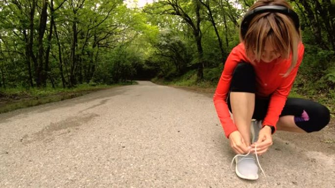一个年轻的高加索女孩坐着绑住鞋带，然后在高加索的森林道路上慢跑。广角