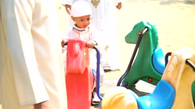 穆斯林家庭让儿子早上在公园的旋转木马上玩耍