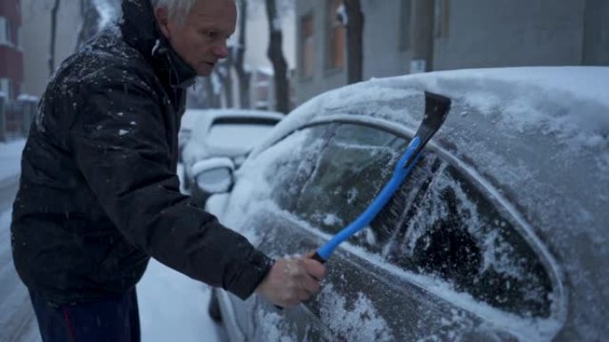穿着冬季夹克的老人在屋前的停车场上清洁汽车