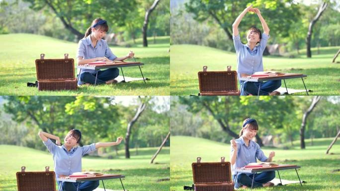 年轻美丽的亚洲女人在笔记本上写字，在大自然或公园和阳光中伸展自己。新鲜快乐的放松。慢动作
