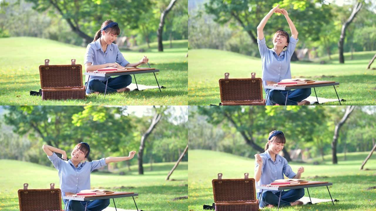 年轻美丽的亚洲女人在笔记本上写字，在大自然或公园和阳光中伸展自己。新鲜快乐的放松。慢动作