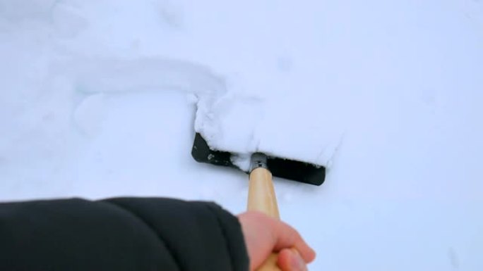 男人从小路上铲雪。暴风雪后用雪铲从人行道上除雪。雪块。