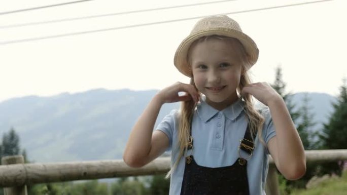 戴着帽子的可爱女孩在群山的背景下微笑。