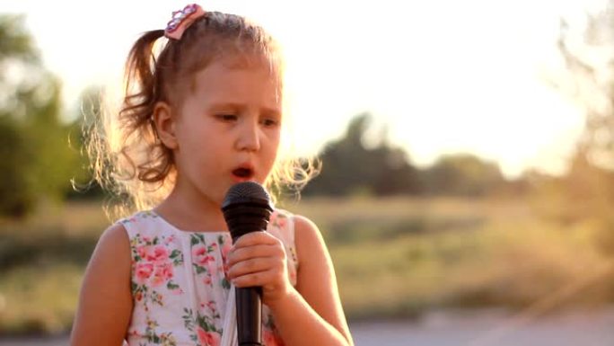 小女孩在夏天的夕阳中对着麦克风唱歌。有才华的孩子是一个音乐的声音。