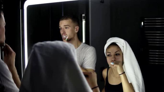 年轻的情侣在室内刷牙时照镜子。头上戴着浴巾的女士