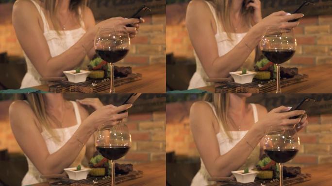年轻女子在烧烤餐厅晚餐时使用智能手机。女人在肉店晚餐时用手机浏览网络