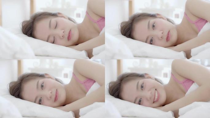 美丽的肖像年轻的亚洲妇女在早安日出醒来时躺着微笑，女孩在卧室里快乐，生活方式和放松概念，慢动作。
