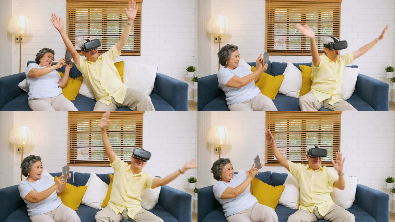 亚洲老年夫妇玩虚拟现实眼镜耳机和平板电脑看vr视频，在家里的客厅沙发上玩得开心。有技术的老年人。在家