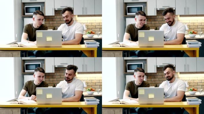 两个家伙在家里的厨房里使用一本教科书学习和在项目上的计算机上工作。互相交谈。