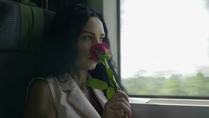 浪漫的年轻女子闻到玫瑰，在火车上离开的窗外看起来很体贴
