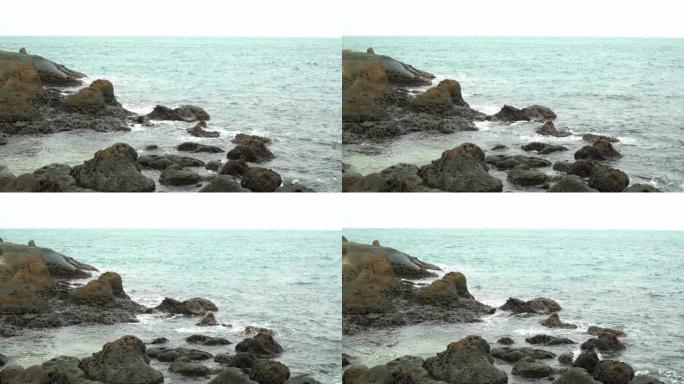 4k视频镜头平移拍摄海浪撞向多岩石的海岸。海浪溅到石头上，溪流猛烈流过许多岩石。