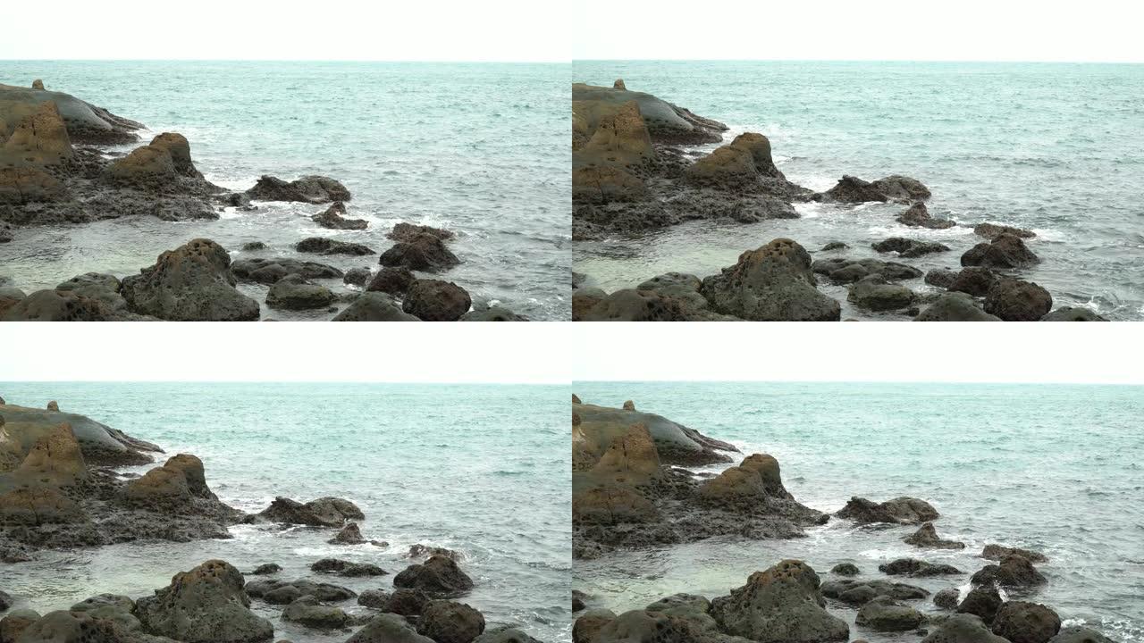 4k视频镜头平移拍摄海浪撞向多岩石的海岸。海浪溅到石头上，溪流猛烈流过许多岩石。