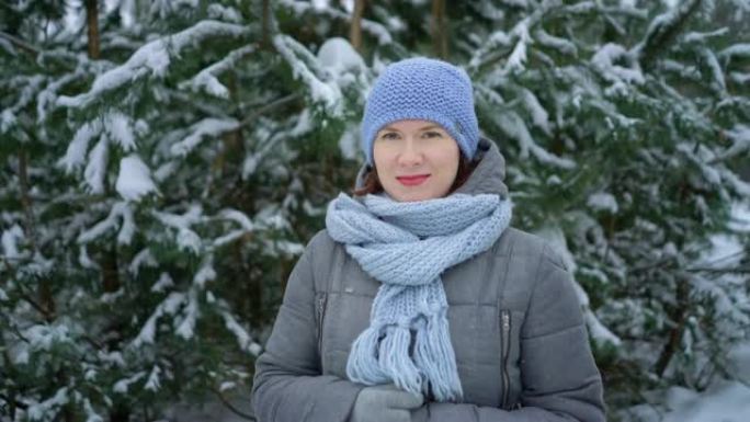 女人在白雪皑皑的冬季森林中的松树中行走时看着相机