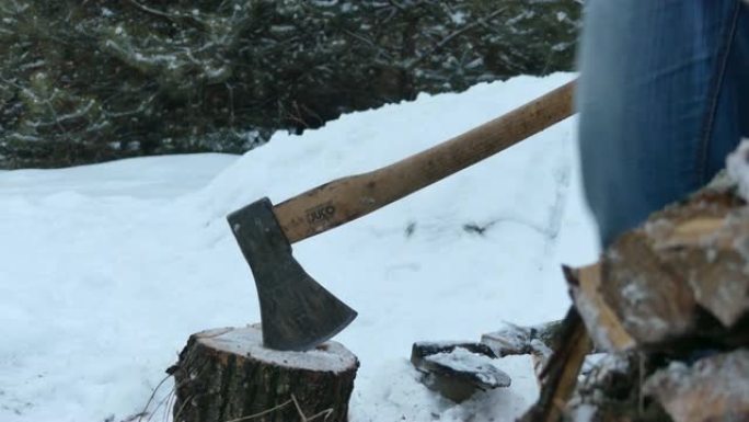 冬天，一个大胡子的人在私人住宅的院子里用斧头砍柴。一名男子在冬天为房屋供暖准备柴火。