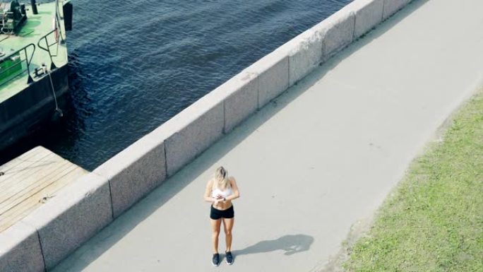 女运动员沿着河边的堤岸奔跑的高角度，停下来检查智能手表上的距离和速度，并进行马拉松训练
