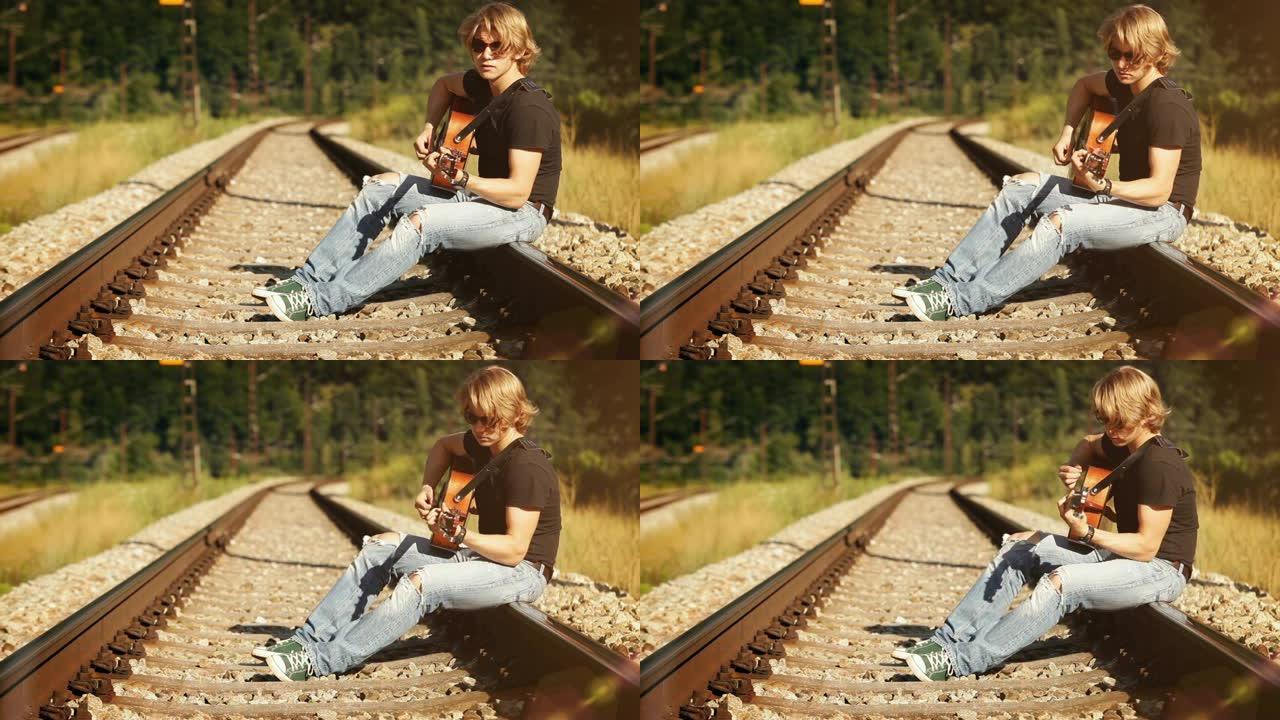 年轻男吉他手坐在铁路上演奏