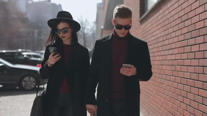 时尚夫妇低头看着他们的智能手机沿着城市街道行走