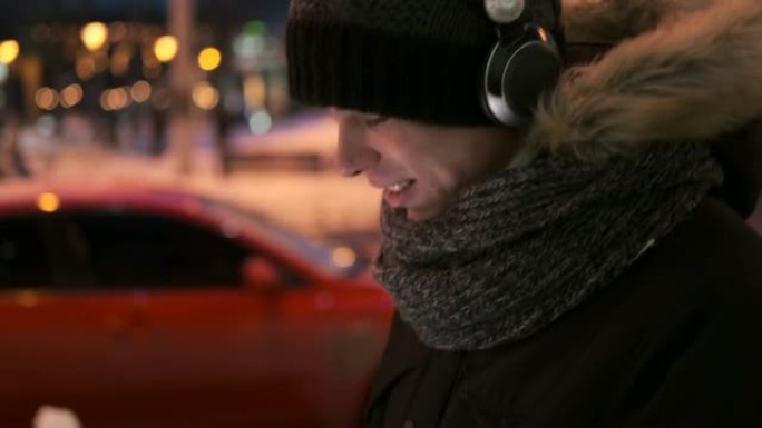 男人在寒冷的冬夜用耳机和手机app听音乐