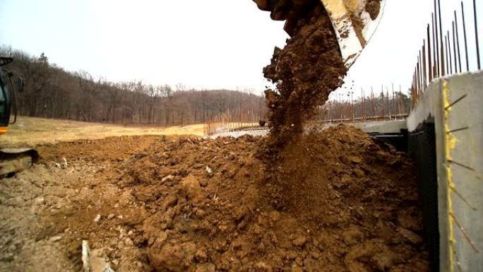 一个抛出地球的挖掘机铲斗的特写镜头。挖掘机挖坑扔泥土的慢动作。广角镜头拍摄