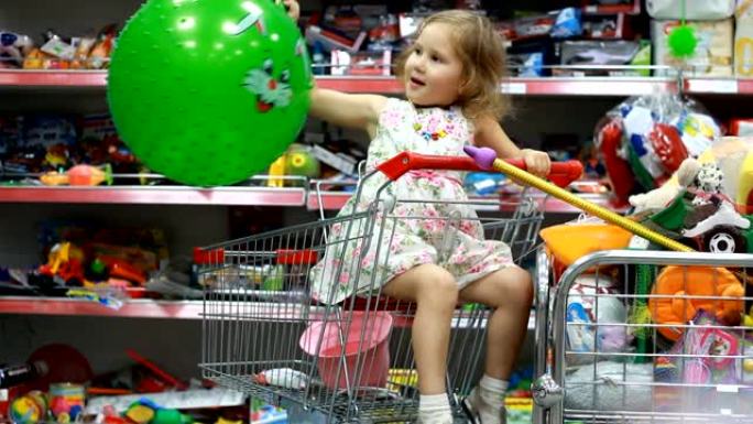 带玩具的儿童商店。超市里的一个孩子坐在购物车里，玩一个绿色的球。