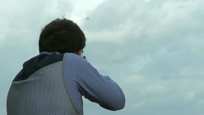 一名男子向一只黏土鸽子发射猎枪，击中目标。