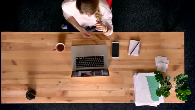 多莉拍摄了在办公室里使用笔记本电脑在视频聊天中闲聊的衣着随意的女人的俯视图。
