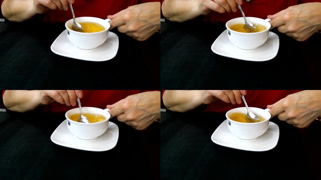 女人的手在白色陶瓷杯中搅拌着新鲜的热茶。