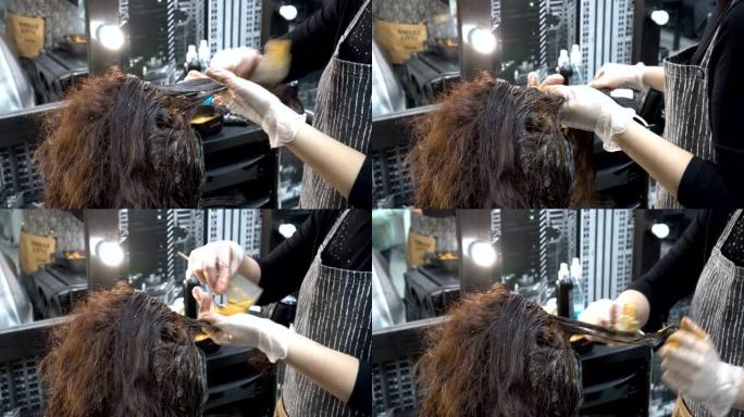 一个女人的头发是在理发店染的。美发师-发型师用刷子将油漆涂在各个股线上。染发程序。头发护理。后视图。