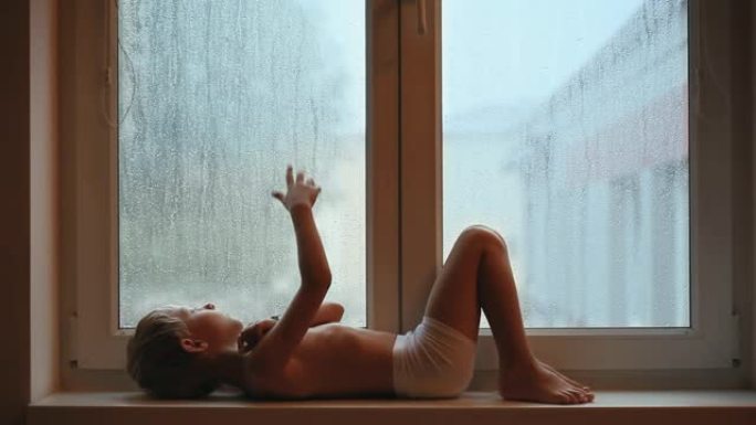 窗台上的悲伤男孩看着玻璃上的雨滴